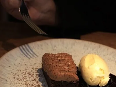 Dessert mit einer Nocke Eis auf dunklem Spiegel, daneben eine Gabel
