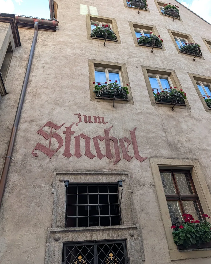 Der Schriftzug Zum Stachel in roter Fraktur an der Fassade des Weinhauses, darüber Fenster mit roten Geranien